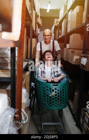 Alberne Lagerarbeiter, die Spaß haben, Mann, der mit der Frau den Wagen schiebt Stockfoto