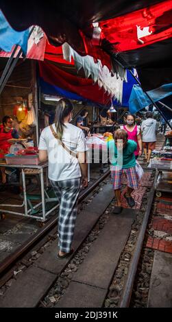 Touristen und Besucher machen ihren Weg entlang der Bahngleise auf dem Mae Klong Railway Market südlich von Bangkok. Stockfoto