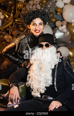 Emotionale Nahaufnahme Portrait DJ Santa Claus mit Sonnenbrillen und Kopfhörer Hören zu Weihnachten Musik und Snow Maiden Schwarz Lederjacke Spaß haben. Rockparty Time. Stockfoto
