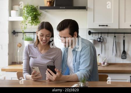 Glückliches junges Paar mit Smartphones, sitzen am Tisch in der Küche Stockfoto