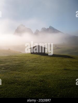 Heuscheune und Hütten auf nebligen Wiesen vor Langkofel und Plattkofel, Morgenlicht, Seiser Alm, Südtirol, Italien Stockfoto