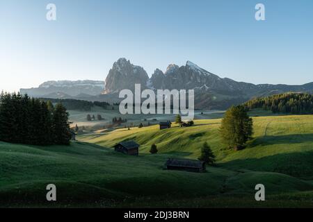 Heuscheune und Hütten auf nebligen Wiesen, hinter Langkofel und Plattkofel, Seiser Alm, Südtirol, Italien Stockfoto