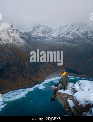 Mann, der auf einer Aussichtsplattform auf einem Berg vor dem Kvalvika Strand sitzt, Fredvang, Lofoten, Norwegen Stockfoto