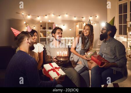 Lächelnde Freunde sitzen und feiern Geburtstag Urlaub Kuchen und Geschenk Boxen Stockfoto