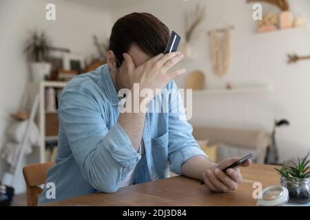 Nahaufnahme deprimierter junger Mann mit Kreditkarte und Smartphone Stockfoto
