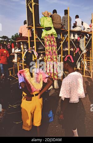 1990er Trinidad und Tobago - der Moko Jumbie (auf Stelzen) beobachtet Hertiage Festival-Darsteller, wie Kinder auf ca. 1993 Stockfoto