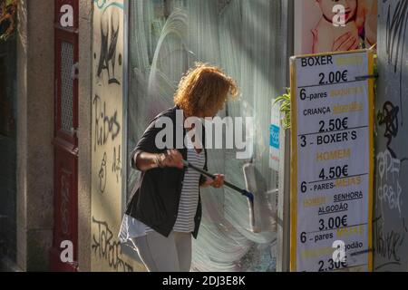 PORTUGAL, PORTO - 5. SEPTEMBER: Porto ist die zweitgrößte Stadt Portugals. Frau waschen Glas von Shop im Freien am 5. September 2016, Porto, Portugal. Stockfoto