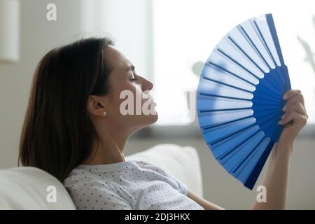 Nahaufnahme überhitzte junge Frau winkt blauen Papierventilator Stockfoto
