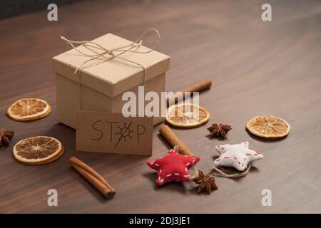 Weihnachts-Geschenkbox aus umweltfreundlichem Papier mit Naturgarn auf Holztisch mit natürlichen Dekorationen und Stoppkarte verpackt, flacher Fokus