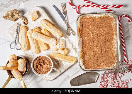 Italienische Tiramisu von Marienkäfer, Espresso und Mascarpone Käse mit serviert auf einem Glasbehälter mit Zutaten auf einem weißen Marmorboden mit ch Stockfoto