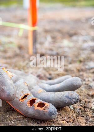 Der gerissene rechte Arbeitshandschuh liegt auf dem Schmutz. Aushubarbeiten. Markierung Holzstift mit Konturzug. Verschlissene Arbeitshandschuhe. Stockfoto