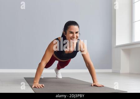 Attraktive Sportlerin hält eine Planke und macht Presseübungen in einem hellen Fitnessstudio. Stockfoto