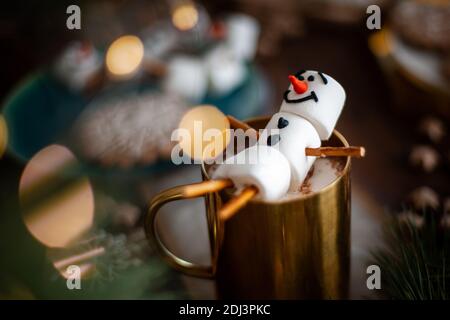 Ein Marshmallow Schneemann mit Glasur dekoriert. Goldbecher mit Kakao- und Weihnachtsdekor. Lebkuchen in Form von Schneeflocken. Stockfoto