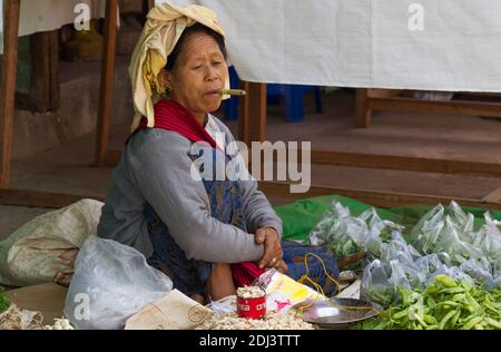 Nyaung Shwe, Myanmar - 24. November 2014: Frau, die Gemüse auf dem lokalen Markt verkauft, raucht eine Zigarre, während sie auf Kunden wartet. Stockfoto