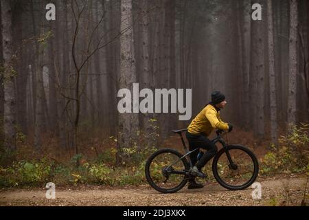 Schöner junger Mann, der beim Radfahren durch den Herbst eine Bremse zieht Wald Stockfoto