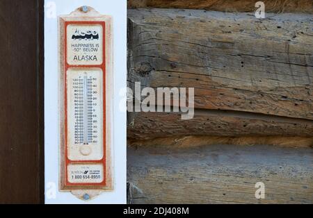 Historisches Thermometer mit der Aufschrift "Glück ist unter 50 Grad - Alaska" auf dem weißen Fensterrahmen eines Holzhauses montiert. Stockfoto