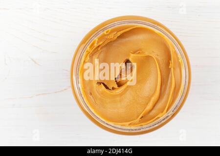 Glas Erdnussbutter auf weißem Holztisch. Leerzeichen für Text. Draufsicht. Stockfoto
