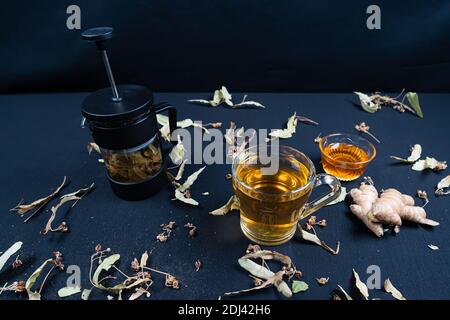 Französische Presse und Kräutertee, auf schwarzem Hintergrund zwischen trockenen Blättern Stockfoto