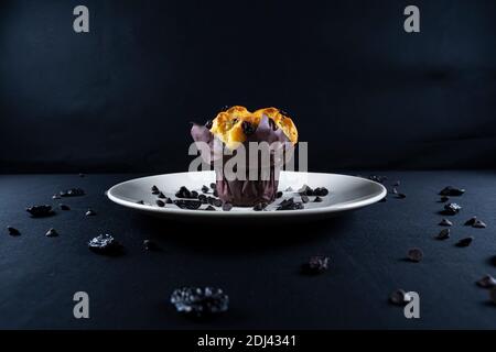 Schokolade, Rosinen-Chips und Schokolade Rosinen-Muffin auf einem weißen Teller. Schwarzer Hintergrund. Copyspace Stockfoto