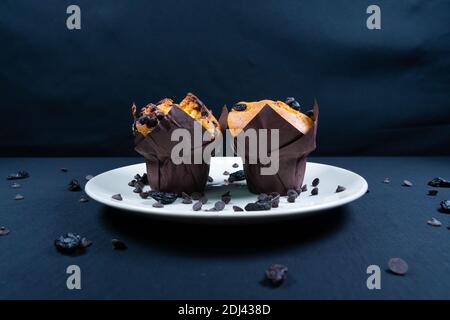 Schokolade, Rosinen-Chips und Schokolade Rosinen-Muffin auf einem weißen Teller. Schwarzer Hintergrund. Copyspace Stockfoto