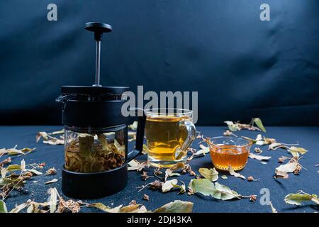 Französische Presse und Kräutertee, auf schwarzem Hintergrund zwischen trockenen Blättern Stockfoto