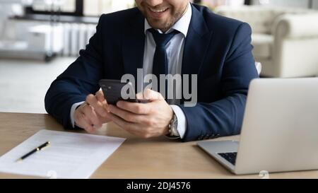 Nahaufnahme erfolgreicher lächelnder Geschäftsmann mit Smartphone, am Schreibtisch sitzend Stockfoto