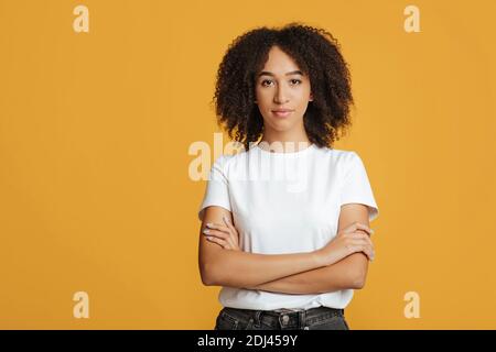 Ernst selbstbewusst junge afroamerikanische Frau mit lockigen Haaren in Weißes T-Shirt mit gekreuzten Armen Stockfoto