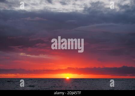 Dramatischer Sonnenuntergang über dem Meer mit beeindruckenden orangen und grauen Wolken. Stockfoto