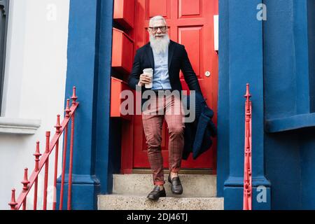 Hipster Senior Mann trinken Kaffee, während Sie mit zu Hause gehen Tür im Hintergrund - Fokus auf Gesicht Stockfoto