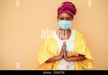 Ältere schwarze Frau hält die Hände in Gebetsstellung und trägt traditionell afrikanisches Kleid - Soziales Fernkonzept Stockfoto