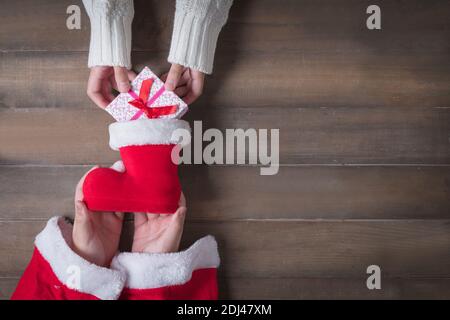 Kind Hand schickte Geschenk in Weihnachtsmann Schuhe am Weihnachtstag. Alter Holzhintergrund mit Kopierraum. Stockfoto