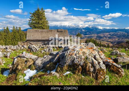 Malerische Frühling ländliche Landschaft mit alten Holzhütte und hohen schneebedeckten Bergen im Hintergrund, Siebenbürgen, Rumänien, Europa Stockfoto