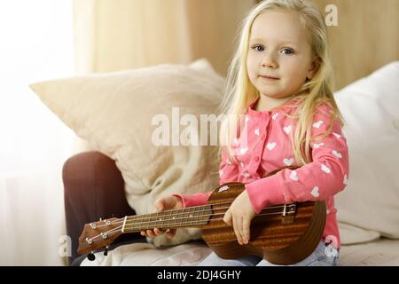 Kleine niedliche Baby spielen Ukulele gitarre im sonnigen Zimmer. Kinderkonzept Stockfoto