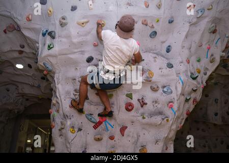 Aktiver sportlicher Mann mit Hut üben Klettern auf Kunststein in einer Kletterwand. Extremsportkonzept. Stockfoto