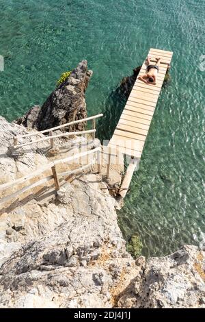 Ein Mann, der auf einem kleinen hölzernen Pier am Preveli Beach, Kreta, Griechenland, Sonnenbaden geht Stockfoto