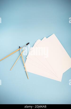 Aquarellpinsel unterschiedlicher Größe liegen zusammen mit Aquarellpapier auf blauem Hintergrund. Zeichenunterricht Stockfoto