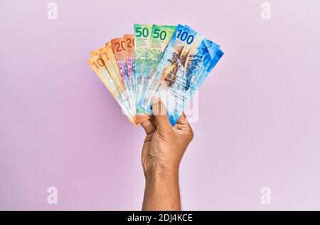 Hispanische Hand hält schweizer Franken Banknoten über isolierten rosa Hintergrund. Stockfoto