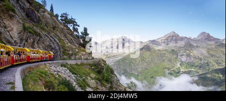 Touristenzug voll von Menschen durch eine Bergschlucht in den Pyrenäen, Wolken im Tal unter den Bergen, Artouste Frankreich, Panorama Stockfoto