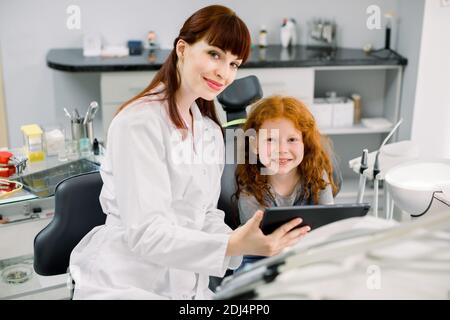 Medizin, Kinderzahnheilkunde und Mundpflege Konzept. Lächelnde Zahnärztin zeigt Tablet-pc-Computer glücklich Kind Patienten, lockig rothaarige Schule Stockfoto