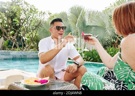 Fröhliche Paar Toasting mit süßen erfrischenden Cocktails, wenn Sie Urlaub Am Pool im Spa-Hotel Stockfoto