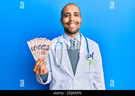Hispanic erwachsenen Arzt Mann trägt medizinische Uniform hält 500 mexikanische Pesos schauen positiv und glücklich stehen und lächeln mit einem Selbstbewusstes Lächeln sho Stockfoto