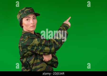 Frau in Militäruniform schaut auf die Kamera und zeigt den Zeigefinger nach oben. Grüner Hintergrund. Stockfoto