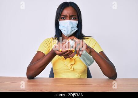 Junge afroamerikanische Frau trägt medizinische Maske hält Hand Desinfektionsmittel Gel skeptisch und nervös, runzelte wegen des Problems. Negative Person. Stockfoto