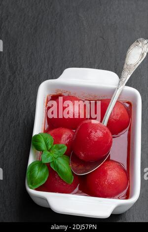 Hausgemachte geschälte Tomaten in Tomatensaft in Keramikschale auf Schwarzer Stein Hintergrund Stockfoto