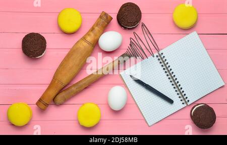 Der Prozess der Herstellung von Schokoladenkeksen, Makronen, Zutaten auf einem rosa Holzhintergrund. Eier, Nudelholz, Corolla, Rezept Notizbuch mit einem Stift. T Stockfoto