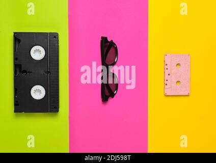 Videokassette, Sonnenbrille, Audiokassette auf mehrfarbigem Papierhintergrund. Minimalistischer Trend, flach liegend, Draufsicht. Stockfoto