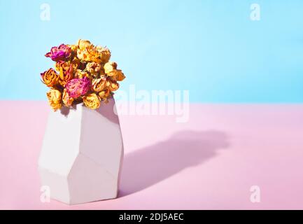Trockene Blumen wilde Rosen in der weißen Steinvase auf dem Tisch. Harte Schatten. Stockfoto