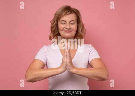 Yoga und Meditation. Ältere Frau, die während der Meditation die Augen geschlossen hält, ruhig und friedlich ist und die Hände in Mudra-Geste hält. Stockfoto