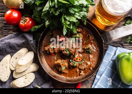 Ungarischer Gulasch in einer Schüssel mit Paprika, Tomaten, Kräutern, Knödeln und einem Bier vom Fass. Stockfoto