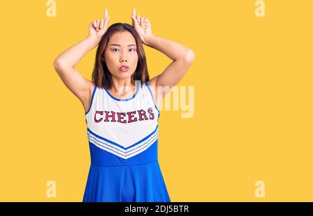 Junge schöne chinesische Mädchen trägt Cheerleader Uniform tun lustige Geste Mit Finger über Kopf als Stierhörner Stockfoto